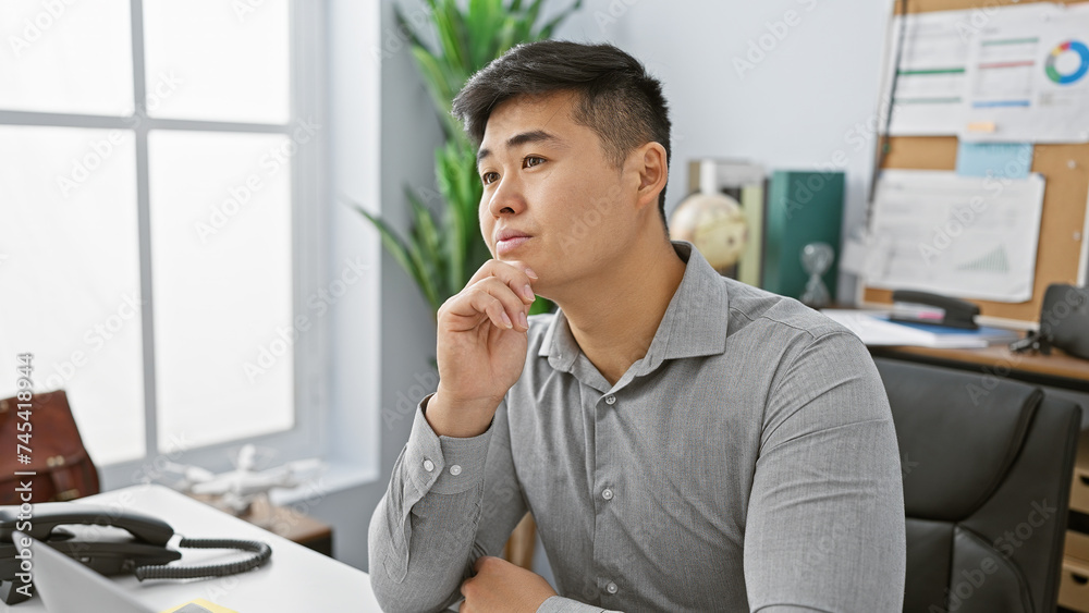 A contemplative young asian man in an office setting with a focus on business and professionalism, exuding a sense of thoughtfulness and career orientation.