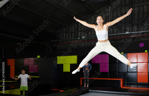 Excited young girl in activewear captured mid-air during fun jump at colorful indoor trampoline center..