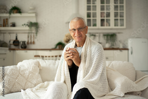 A man with glasses drinks tea and warms himself on the sofa in the kitchen.