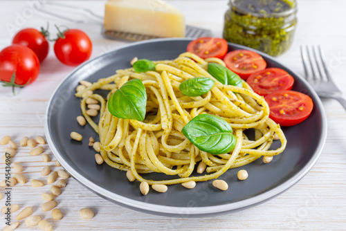 Pasta pesto, spaghetti with pesto sauce and fresh basil leaves in black plate on white wooden background served with food ingredients. Traditional italian cuisine.