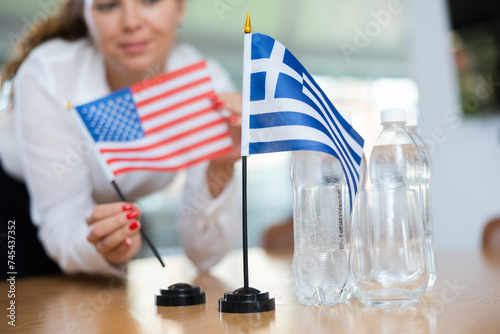 Young female assistant setting up greek and american flags for international negotiations photo