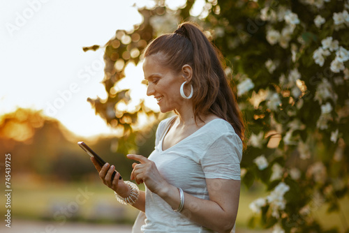 smiling trendy woman in white shirt using smartphone