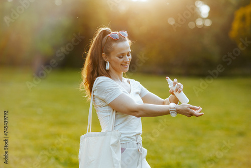 happy trendy woman in white shirt with tote bag using spf