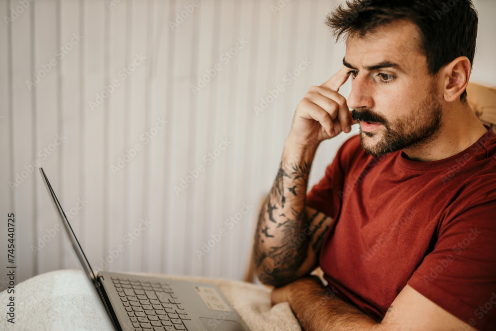 Man in pajamas starting his day with technology, using laptop and smartphone in bed Man in pajamas starting his day with technology, using laptop and smartphone in bed