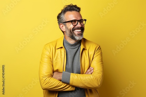 Portrait of a happy senior man in yellow jacket and eyeglasses over yellow background © Asier