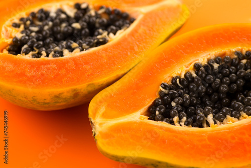 Papaya fruits on orange, yellow background. Halved fresh organic Papaya exotic fruit design, close up. Healthy vegan food 