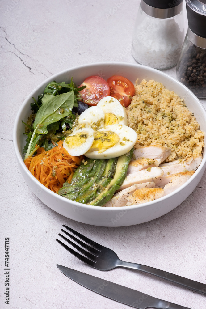 A bowl of couscous, meat, eggs and vegetables angle view on grey background.