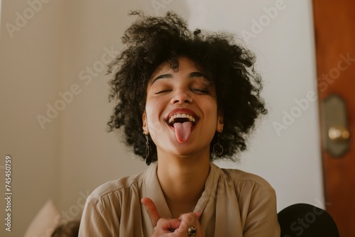 A woman sticks out her tongue with a funny expression, hands clasped.