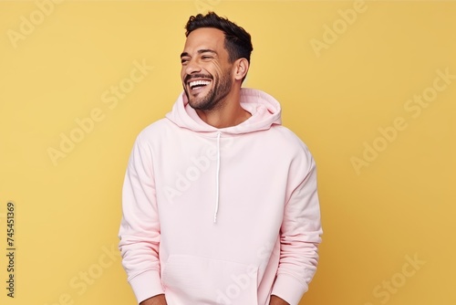 Portrait of happy young man in pink hoodie standing against yellow background