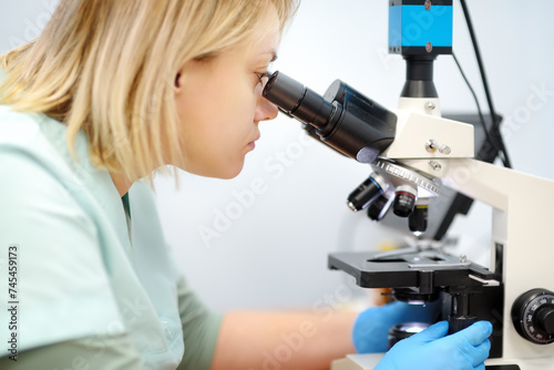 Young female scientist chemist or biologist analyzing new substance or virus in microscope. Woman in a laboratory for medical, forensic or microbiological research. Lab for pharmaceutical development