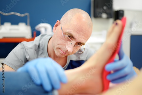 Orthopedic insoles. Fitting orthotic insoles. Flatfoot treatment. Podiatry clinic. Male orthopedist tries insole on patient's foot in clinic. photo