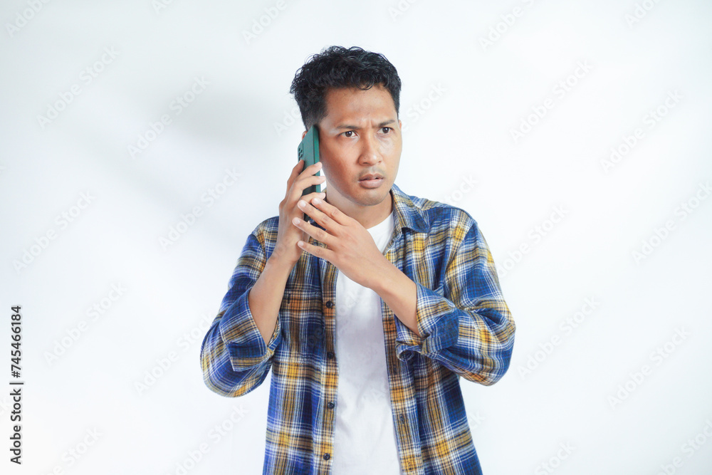 Adult Asian man showing worried expression during a phone call Adult Asian man showing worried expression during a phone call