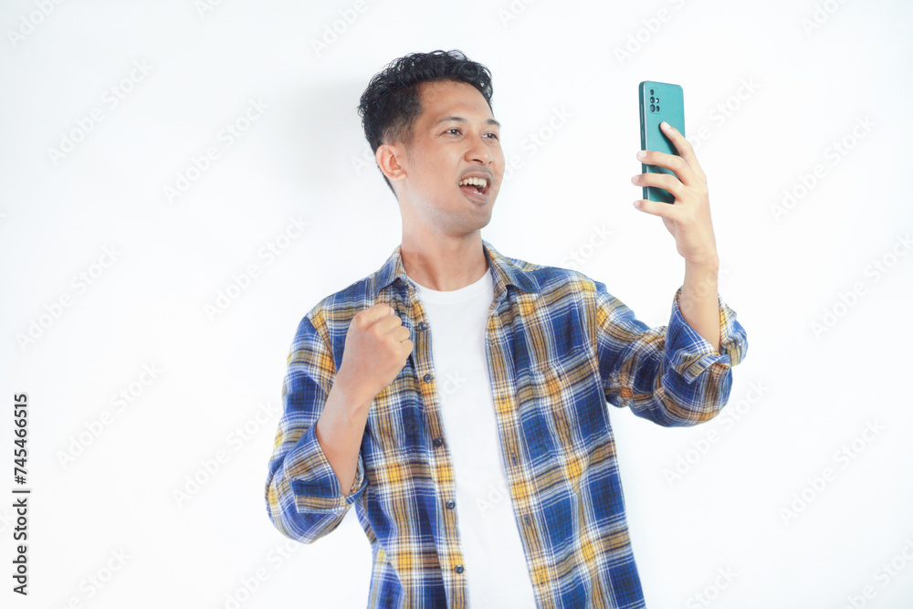 Adult Asian man showing happy gesture while looking to his mobile phone Adult Asian man showing happy gesture while looking to his mobile phone