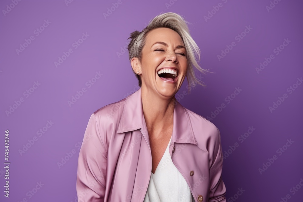 Portrait of a beautiful middle-aged woman laughing and looking away against purple background