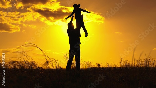 Dad plays with his child son  throws child up into sky with his hands  happy child smiles. Father child son  play together in park in front of sun  Silhouette. Family happiness concept . Child is fly