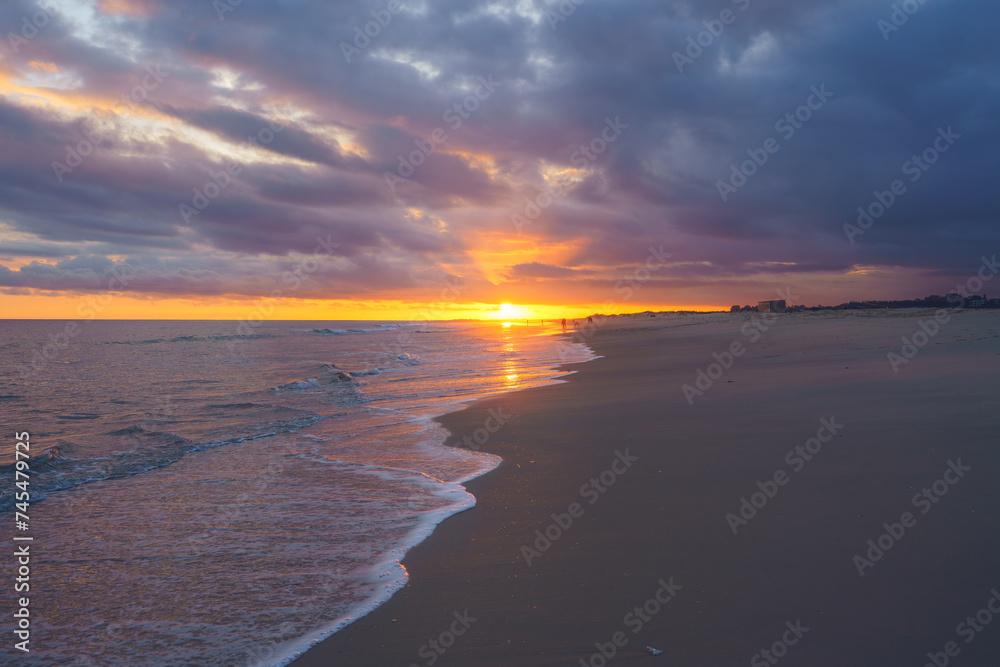 Dramatic sunset skies blaze with color over a peaceful beach, casting reflections on the wet sand