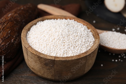 Tapioca pearls in bowl and cassava roots on wooden table, closeup