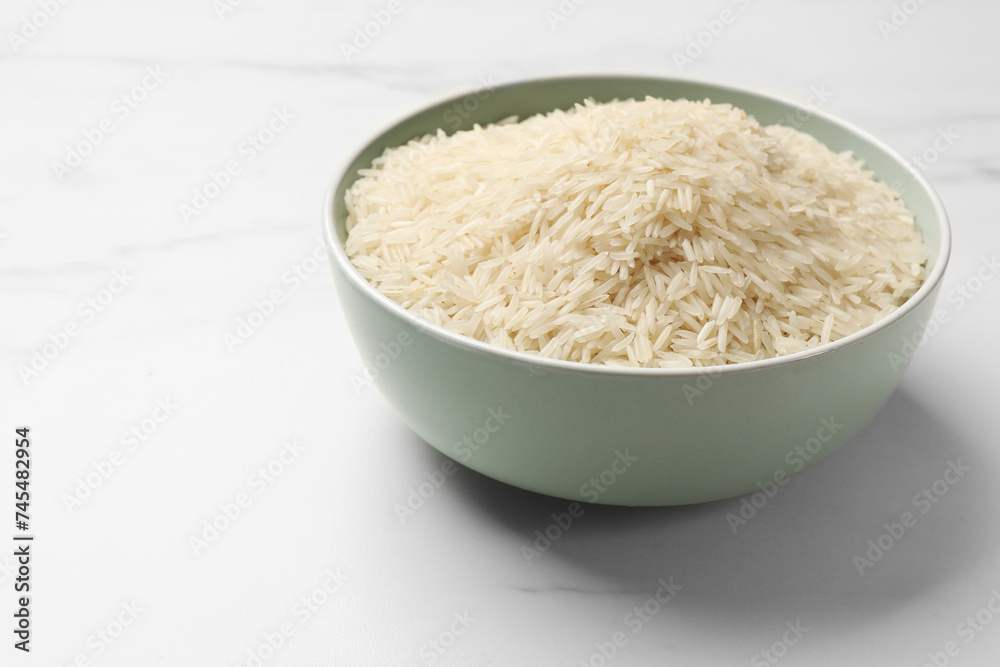 Raw basmati rice in bowl on white marble table, space for text Raw basmati rice in bowl on white marble table, space for text