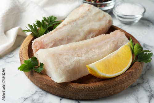 Fresh raw cod fillets with parsley and lemon on white marble table, closeup