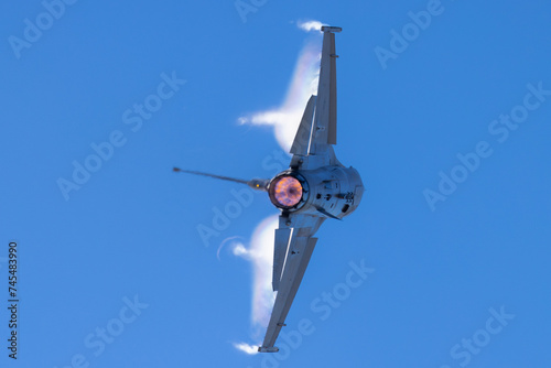 Close tail view of a F-16 Fighting Falcon in a high G maneuver, with condensation streaks at the wing roots and tips, and afterburner on 