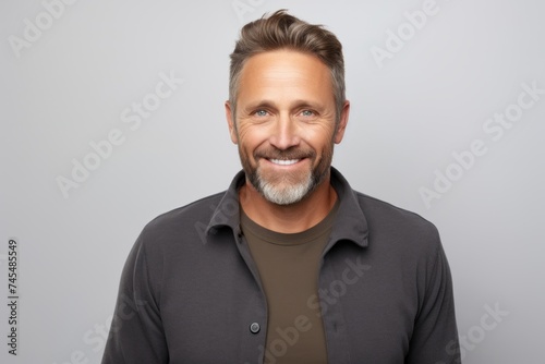 Handsome mature man in casual clothes smiling at camera while standing against grey background