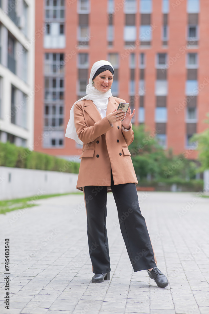 Young woman in hijab using smartphone outdoors. 