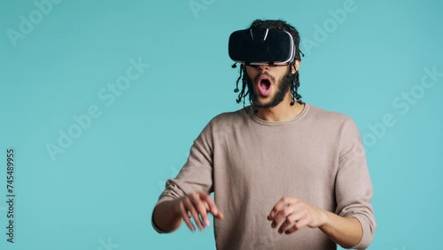 Tech enthusiast wearing virtual reality goggles, doing swiping gestures. BIPOC man using high tech futuristic modern VR glasses, making tactile touching gesturing, blue studio background photo