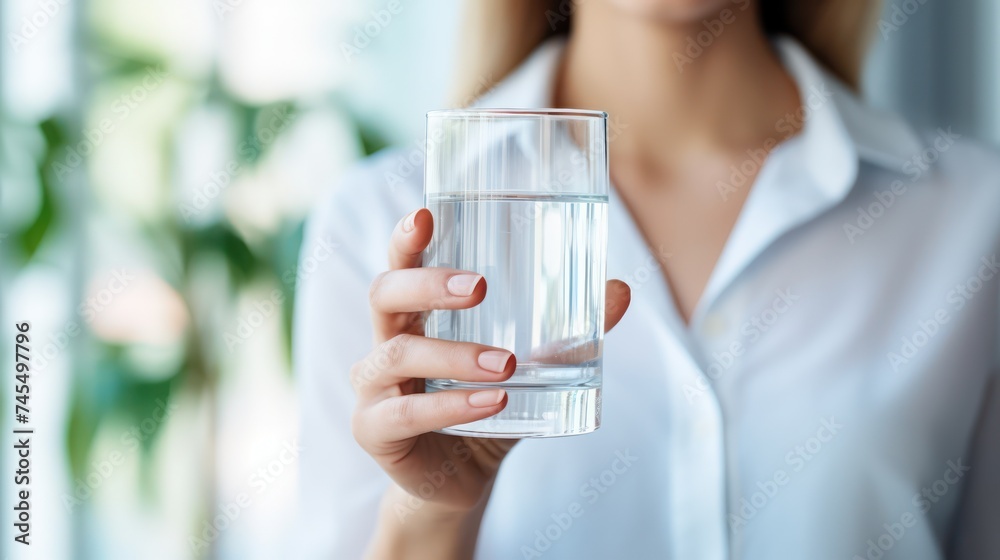 A Health concept. Horizontal banner image, on foreground caucasian female hand holds glass of clear water give to camera smiling selective close up focus. A Health concept. Horizontal banner image, on foreground caucasian female hand holds glass of clear water give to camera smiling selective close up focus.