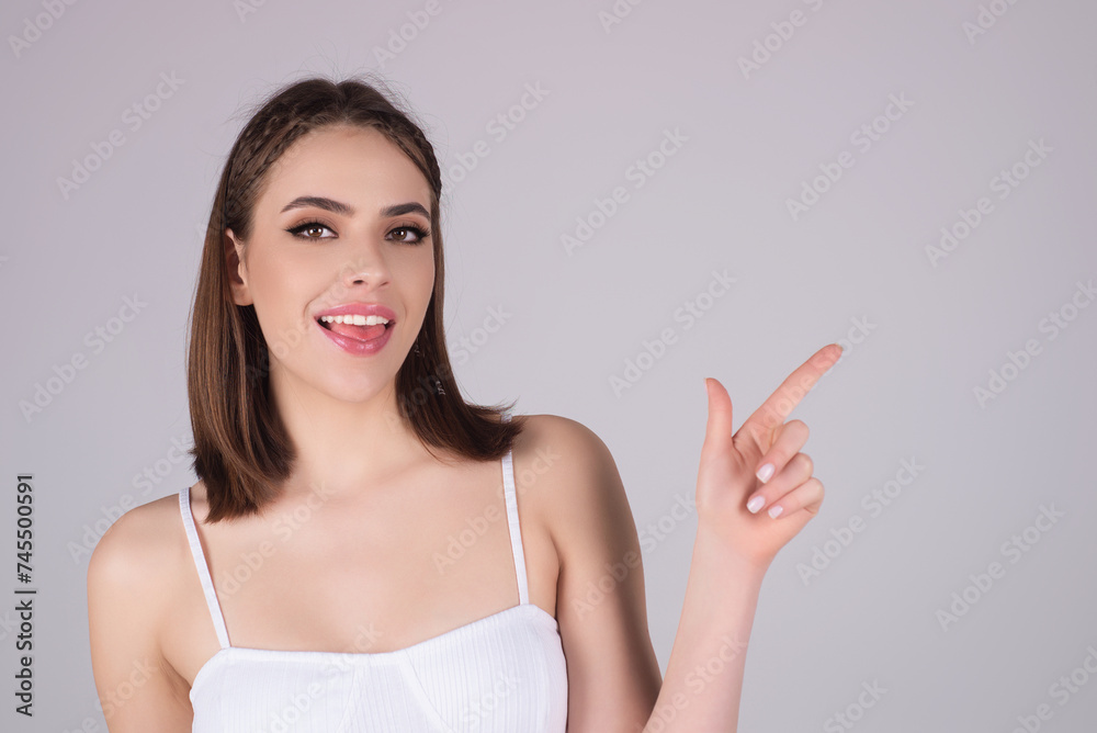 Young happy woman pointing copy space. Studio close up portrait of Girl looking at camera and pointing away on isolated background. Smiling Girl points a finger away. Young woman showing copy space. Young happy woman pointing copy space. Studio close up portrait of Girl looking at camera and pointing away on isolated background. Smiling Girl points a finger away. Young woman showing copy space.
