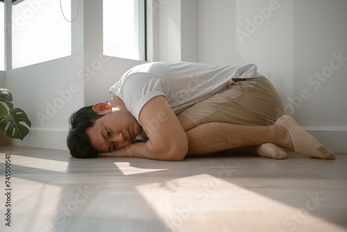 Sad and depressed asian man hugging himself down on the floor.