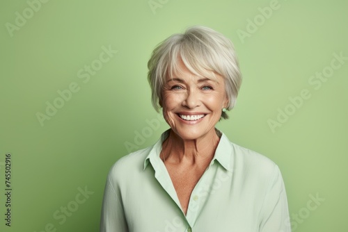 Portrait of a smiling senior woman standing against a green background.