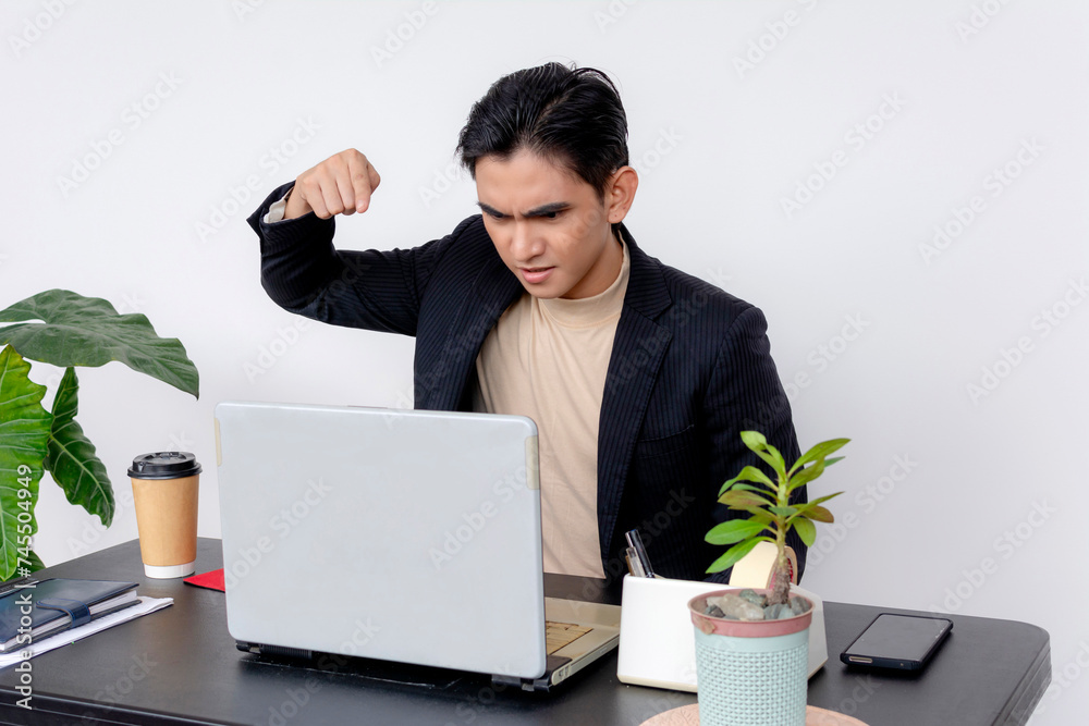 An irate young male office worker showing his fist towards a laptop screen, expressing frustration and anger at work. An irate young male office worker showing his fist towards a laptop screen, expressing frustration and anger at work.