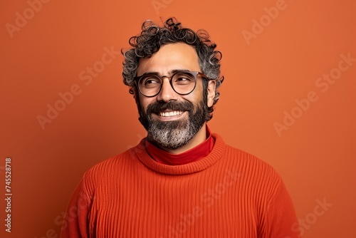 Portrait of a smiling Indian man in red sweater and glasses on orange background © Inigo