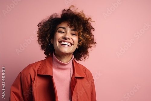 Portrait of a beautiful young woman with curly hair laughing over pink background