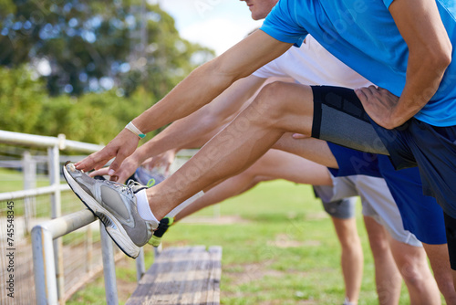 Group, people and outdoor for stretching legs on bench for warm up, workout and training together on grass. Sports, team and exercise on field for health, wellness and fitness in nature with friends