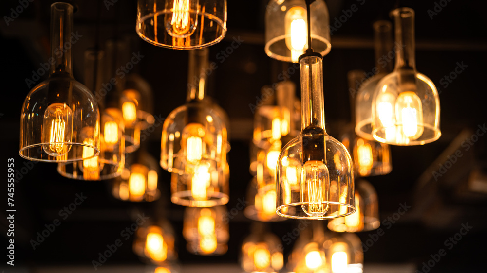 Classic sphere lighting bulbs are glowing in orange warming shade, there are hanging from ceiling in dark environment. Interior cozy style decoration. Close-up and selective focus.