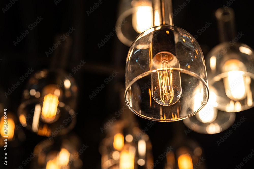 Classic sphere lighting bulbs are glowing in orange warming shade, there are hanging from ceiling in dark environment. Interior cozy style decoration. Close-up and selective focus.