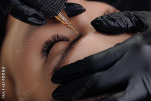 Closeup procedure permanent makeup tattoo for eyebrows of beautiful woman with black brows in beauty salon