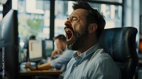 A tired business man letting out a large yawn in the office