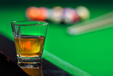 Glass of whiskey on billiard table and billiard balls in background