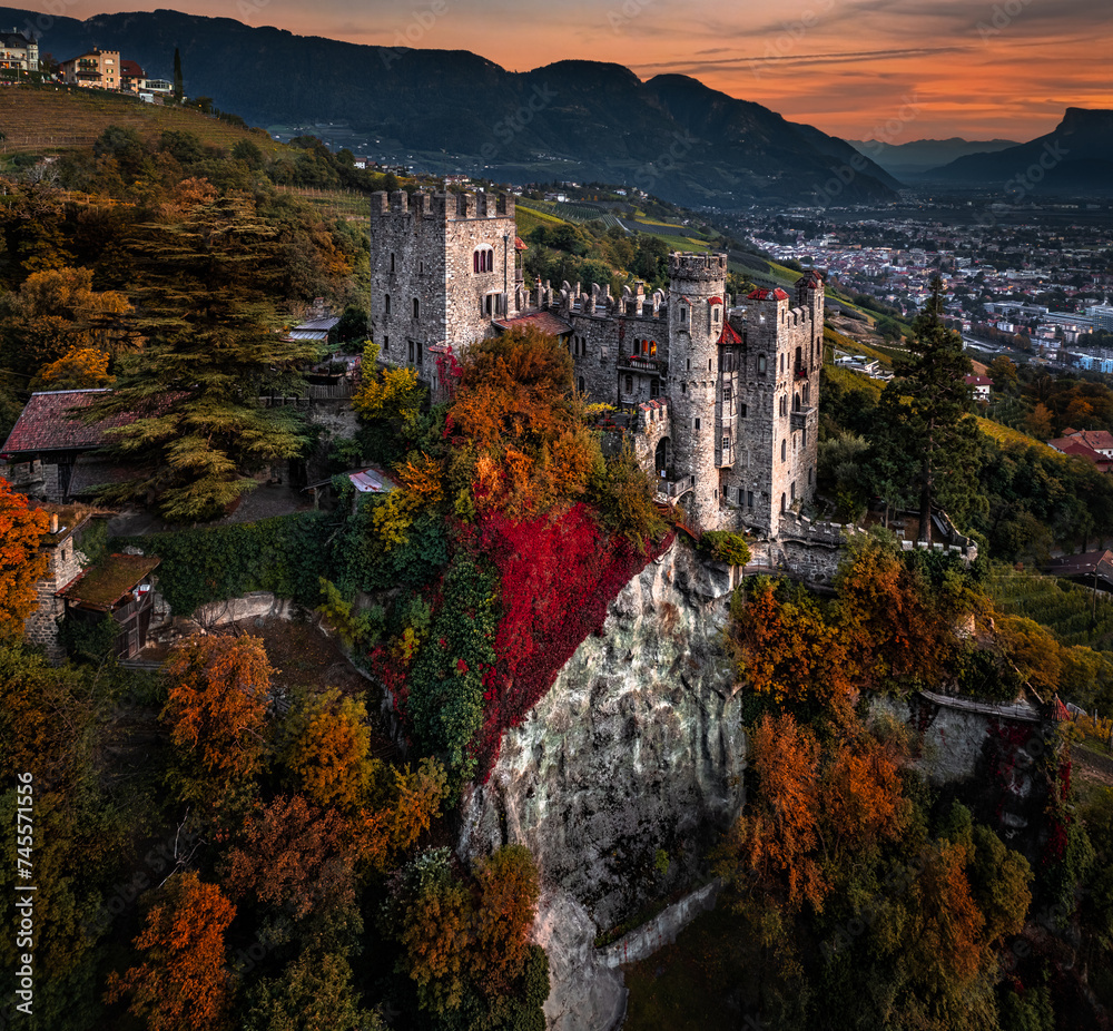 Merano, Italy - Aerial panoramic view of the famous Castle Brunnenburg (Castel Tirolo) with the city of Merano, the Italian Dolomites and colorful sunset sky at background at autumn time - obrazy, fototapety, plakaty 