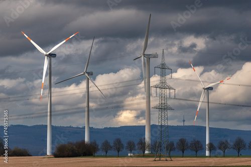 Windräder einer Windkraftanlage in verdichteter Teleaufnahme mit Bergen am Horizont und geschlossener, grauer Wolkendecke photo