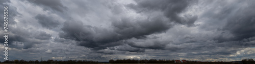 Panoramafoto einer geschlossenen, grauen Wolkendecke mit Gewitter- und Haufenwolken in Unteransicht
