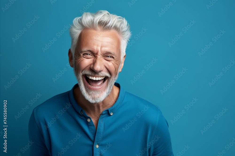 Portrait of a happy senior man laughing and looking at camera on blue background Portrait of a happy senior man laughing and looking at camera on blue background