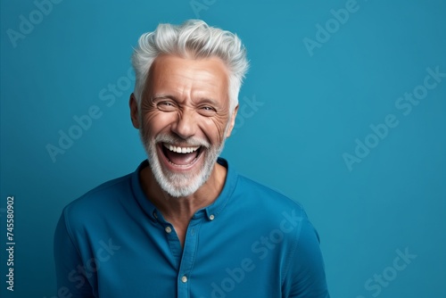Portrait of a happy senior man laughing and looking at camera on blue background