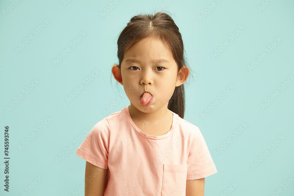 Mischievous Girl Making a Face, Sticking Out Her Tongue Showing to Camera, Studio Portrait Over Blue Isolated