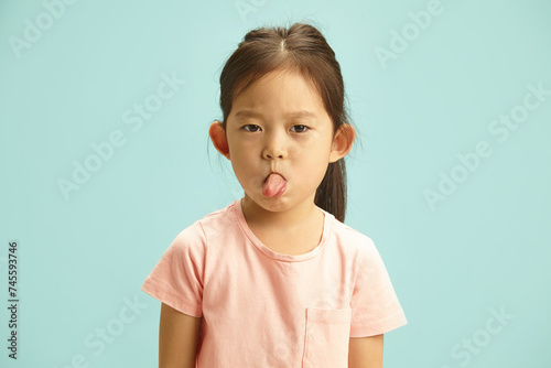 Mischievous Girl Making a Face, Sticking Out Her Tongue Showing to Camera, Studio Portrait Over Blue Isolated