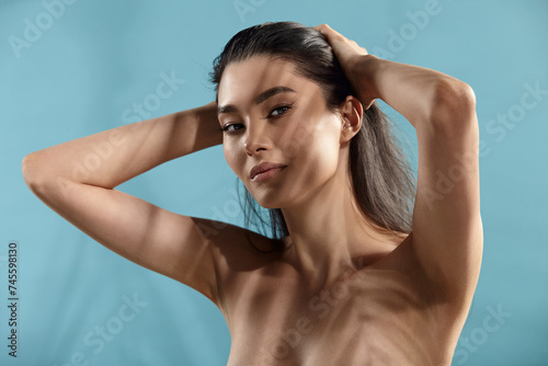 Asian Naked Attractive Woman Holds Hands on Back of Head Using Hair Balm by Hair Care Standing Over Blue Isolated