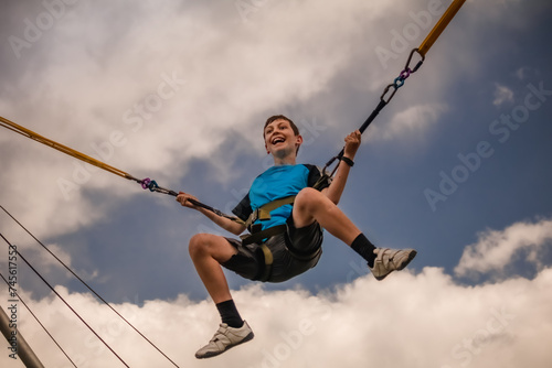 Preteen boy swinging on bungee swing and laughing; sky and clouds in background