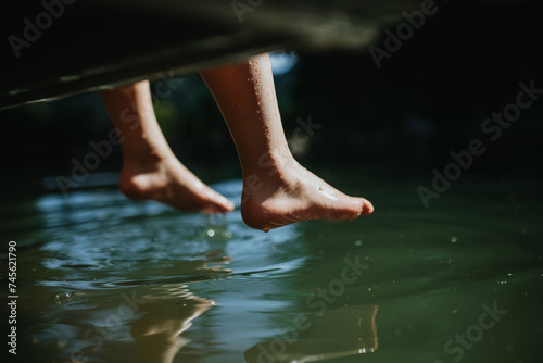 Close-up of kids legs relaxing in lake during hot summer day, top view.